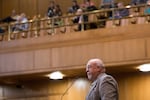 A lawmaker speaks at a microphone in the Oregon state Capitol, with balcony seating visible above him.