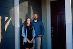 Kaitlyn Morrow and Jeremy Habelitz stand outside of their home in southern California. She is wearing a denim shirt over a black dress and he is wearing a navy button down shirt with khakis.