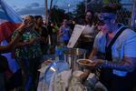 Lorraine Arroyo Román serves "asopao" during a protest against LUMA Energy in Aguadilla, Puerto Rico on Saturday. Román is illuminated by the lights of police vehicles.
