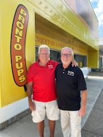 Two men smile straight to camera while standing in front of a Pronto Pups stand.