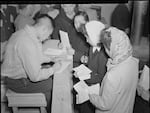 A photo of Japanese American citizens waiting for their absentee ballots to be notarized in 1942 while they were wrongfully incarcerated at the Tule Lake prison camp in California during World War II