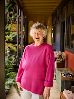 Deana Camp, 73, has curly gray hair and is wearing a bright pink sweater. She is smiling broadly.