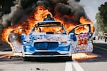 A Waymo car covered in graffiti burns in the street as smoke billows during protests in Los Angeles on Sunday.  