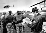 A group watches as a helicopter files low to the ground.