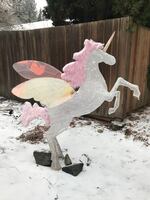 A unicorn yard decoration on its hind legs with wings. The ground beneath it has a dusting of snow.