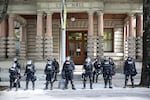 Portland Police in riot gear stand guard in front of Portland City Hall.