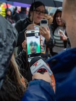 A woman holds a phone with a man's face on it who is speaking over video chat.