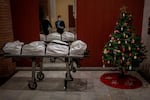 Mortuary workers take off their protective clothing at the entrance of a building decorated with a Christmas tree, after removing the body of person who is suspected of dying from COVID-19 in Barcelona, Spain, Wednesday, Dec. 23, 2020.