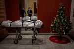 Mortuary workers take off their protective clothing at the entrance of a building decorated with a Christmas tree, after removing the body of person who is suspected of dying from COVID-19 in Barcelona, Spain, Wednesday, Dec. 23, 2020.