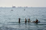 Residents swim and play in the waters of the Strait of Hormuz while cargo ships and commercial vessels lie anchored in the distance off Bandar Abbas, Iran, Wednesday, June 10, 2026.