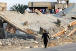 In this photo, a woman dressed in black walks along a road, past the rubble of a collapsed concrete building.