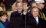 In this Jan. 20, 2001, file photo, standing in the rain, President George W. Bush waves as he watches his inaugural parade pass by the White House viewing stand in Washington, Saturday afternoon, Jan. 20, 2001. With him are his wife and first lady Laura Bush and his father, former President George H.W. Bush.