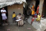 Mahesh Shah, left, stands as his family members look while census worker Rumima Das, writes the information on a paper on the first day of the national census at Ramsingh Chapori village, east of Gauhati, India in 2010.