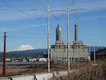 A idle coal plant sits next to a body of water. A snow-capped Mount St. Helens can be seen in the distance.