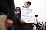 John Spitzberg, 87, wearing glasses and a baseball cap, holds a "Support our Veterans" sign. 