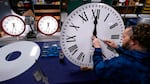 A person fastens the hands to a large white clock.