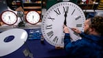A person fastens the hands to a large white clock.