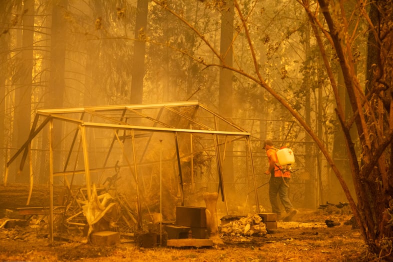 A man puts out spot fires in DeVos' backyard as the Santiam Fire threatens her neighborhood near Gates, Ore., Sept. 9, 2020. "I've never had anyone help me like this before," DeVos said. "I'm just speechless." A portion of her backyard and the front of her home were charred or actively burning Wednesday. The homes around hers were destroyed.