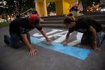 Angela Berry of Olympia, right, and a man who declined to give his name color a blue line under the name "JAY" at Esther Short Park in Vancouver, Wash.