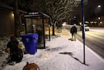 A man waiting for public transit looks down a nearly empty Cesar Chavez Blvd. 