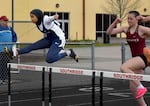 A student in a blue track uniform and black headscarf jumps over a hurdle