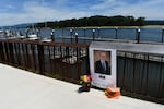 A photo of John Walsh is pasted to a fence near the river, with flowers nearby.