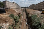 People walk along train tracks running between two high walls. There's trash on the ground all around.