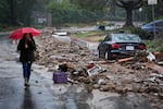 A woman with a red umbrella walks past mud and debris on a street in Studio City, Calif. in 2024. 