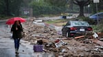 A woman with a red umbrella walks past mud and debris on a street in Studio City, Calif. in 2024.