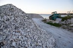 A large pile of oyster shells next to a road with a boat in the background.
