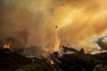 Water is dropped on the advancing Palisades Fire by helicopter in the Pacific Palisades neighborhood of Los Angeles, Tuesday, Jan. 7, 2025.