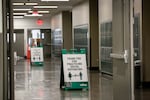 In an empty school hallway, sign boards posted between rows of lockers tell people to practice social distancing.