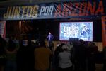 A man in a suit speaks to a crowd while standing under a banner that says "Juntos por Arizona" (Together for Arizona).