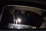 A police officer shines a flashlight as she searches inside a car.