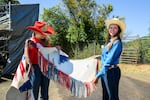 Rodeo competitors Jessica McLennan and Ashlyn Terry hold up McLennan’s chaps at the Benton County Fairgrounds on Tuesday, July 14, 2026. Terry signed the chaps for McLennan.
