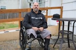 A person sits in a wheelchair and looks at the camera. He has only one leg.