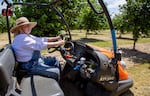 A woman sits on a farm machine in a field of trees.