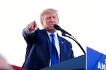 Former President Donald Trump stands at a podium, speaking to and pointing at a crowd.