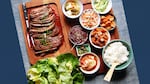 Bison ssam on a cutting board with dishes of accoutrements and rice.