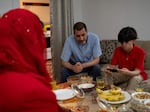 Mujib Ur Rahman plays a video game on a phone in his living room in Lewiston, Maine, while his parents Mohammad Rahmani, center, and Khadija Rahmani, left, talk. The family arrived in Maine in January and are coping with the stresses of a new life in a country where they don't know the language.