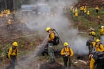 A trainee stands atop a stump spraying water over a burn.