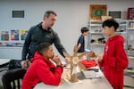 Brandon Rymer, an eighth grade teacher, helps students Braylon, left, and Ben fine-tune a robotic windmill in class.