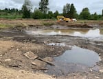 A pond being emptied by a large pump with a backhoe in the distance.