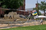A man bicycles with several flags past a helicopter on display during preparations for an upcoming military parade commemorating the Army's 250th anniversary and coinciding with President Donald Trump's 79th birthday.