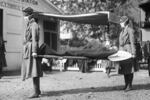 A black and white image shows people in old-fashioned medical attire carrying a sick person on a stretcher.