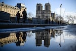 TOPSHOT - Pedestrians pass by the security barriers and fences placed around the Notre-Dame de Paris cathedral on the eve ahead of its official reopening after more than five-year of reconstruction work following the April 15, 2019 fire, in Paris, on December 6, 2024. The Notre-Dame Cathedral is set to re-open early December 2024, with a planned weekend of ceremonies on December 7 and 8, 2024, five years after the 2019 fire which ravaged the world heritage landmark and toppled its spire. Some 250 companies and hundreds of experts were mobilised for the five-year restoration costing hundreds of millions of euros. (Photo by JULIEN DE ROSA / AFP) (Photo by JULIEN DE ROSA/AFP via Getty Images)