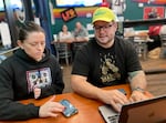 Co-owners Kelli Gilliland, left, and Aaron Gilliland, right, work on an upcoming TV schedule at Icarus Wings and Things in Salem, Ore., on Oct. 20, 2023. Icarus is a restaurant and bar dedicated to gluten-free food and women's sports. The co-owners said it's hard to find a steady stream of women's sports on TV.