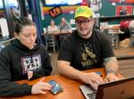 Co-owners Kelli Gilliland, left, and Aaron Gilliland, right, work on an upcoming TV schedule at Icarus Wings and Things in Salem, Ore., on Oct. 20, 2023. Icarus is a restaurant and bar dedicated to gluten-free food and women's sports. The co-owners said it's hard to find a steady stream of women's sports on TV.