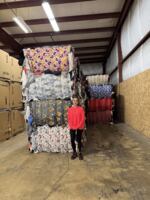 Warehouse Manager Brandi Carter is dwarfed by the huge bales of compacted clothes in St. Vinnie's Seneca textile sorting warehouse in West Eugene.