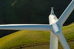 An overhead view looking down on the blades of a wind turbine and the terrain below it.